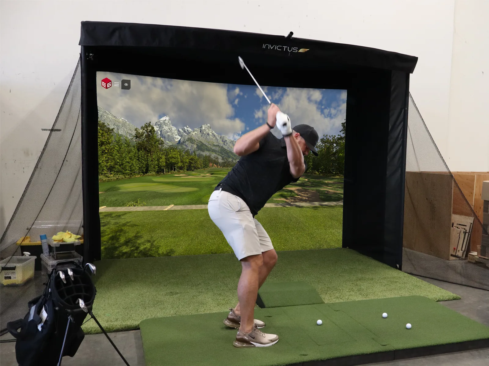 Golfer mid-swing in a portable Invictus simulator booth at an indoor event